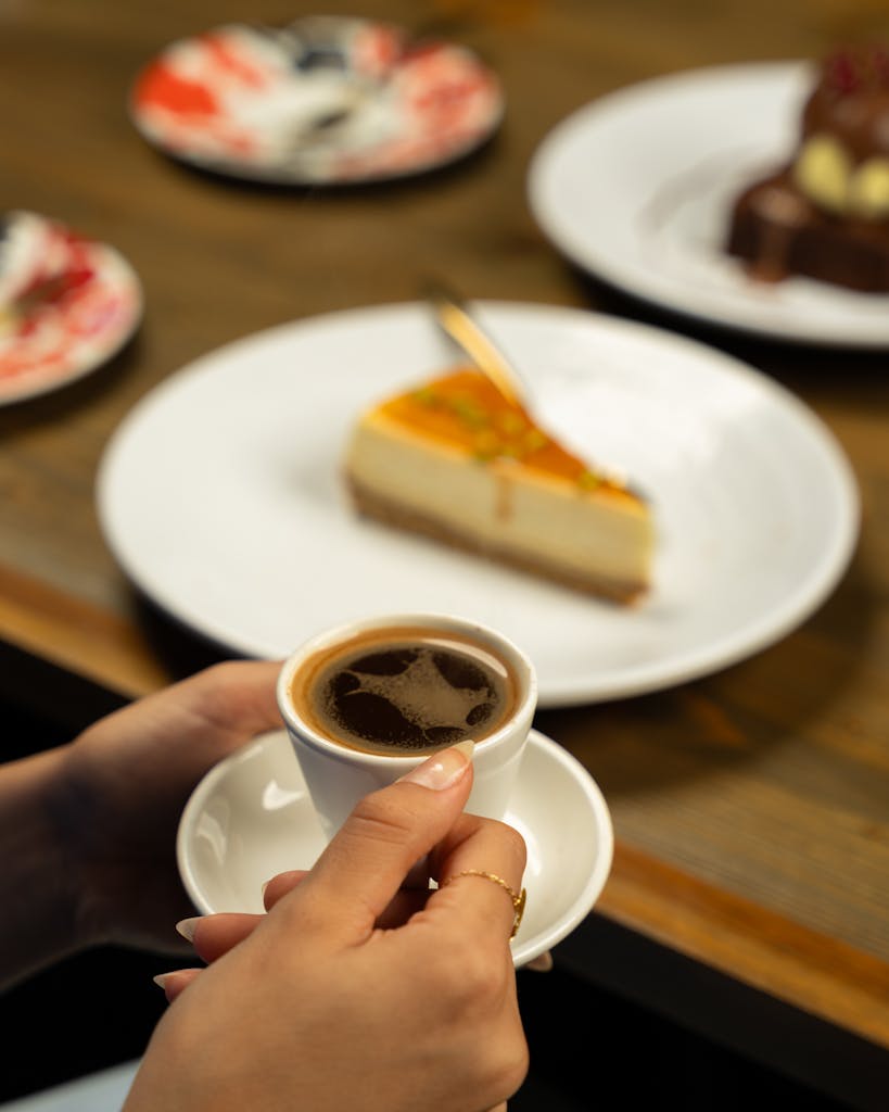 A person holding a cup of coffee and a slice of cake