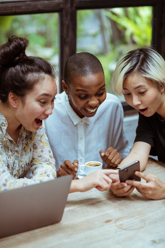 Un groupe de femmes assises autour d'une table, regardant un téléphone, une tasse de café à la main