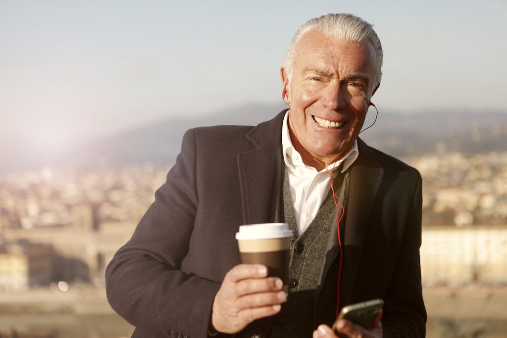 Elderly man smiling with coffee cup in hand, enjoying an outdoor setting.