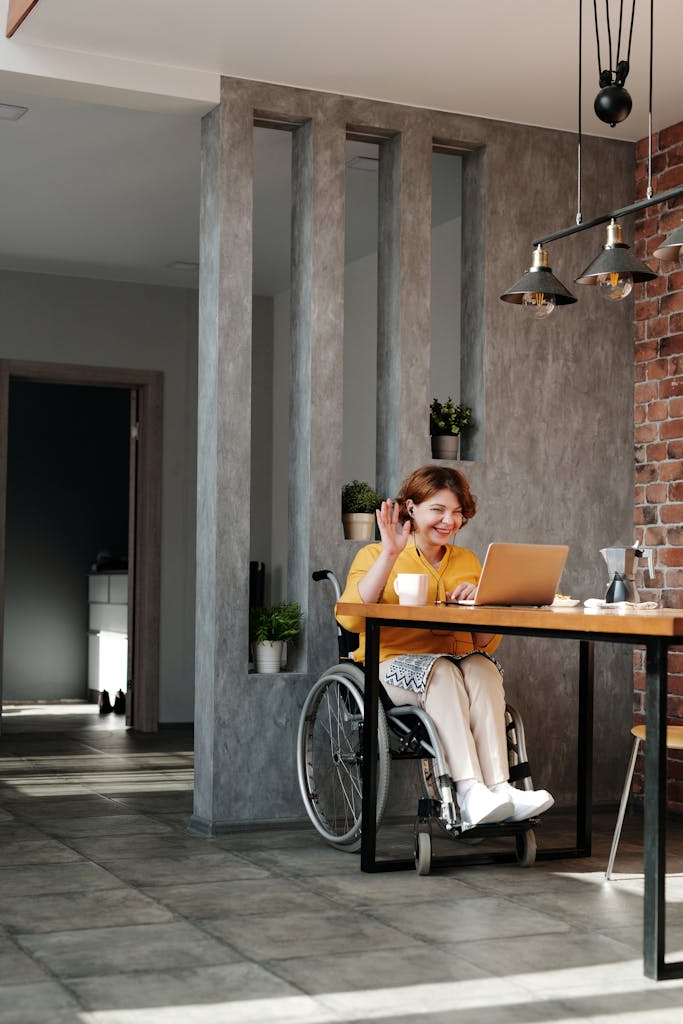 Woman in a wheelchair enjoying remote work and video call at home in a modern interior.