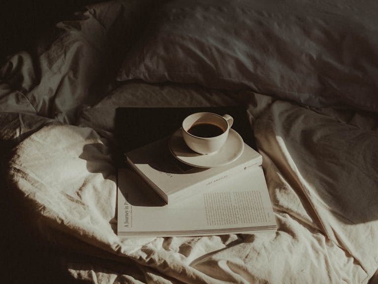 A warm morning scene with coffee cup and books on a cozy bed.