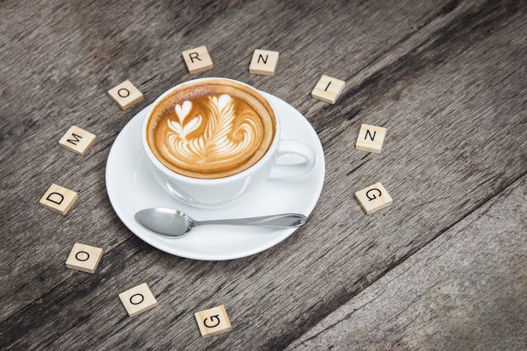 Cup of cappuccino with latte art surrounded by Scrabble letters spelling 'Good Morning'.