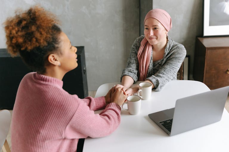 Two women sharing a supportive conversation over coffee indoors. One woman wears a head wrap.