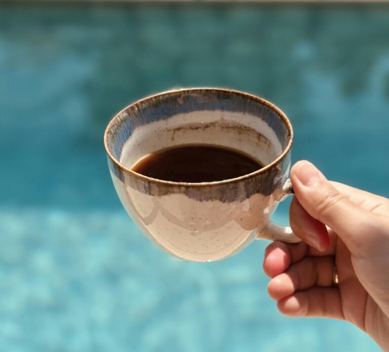 A serene scene of a hand holding a coffee mug by a clear blue pool, embodying relaxation and summer vibes.