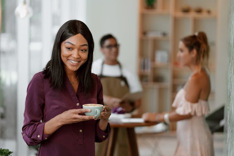 A woman smiling while holding a coffee cup in a modern indoor cafe setting.