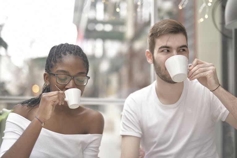 Interracial couple enjoying coffee in a relaxed indoor setting, sharing a moment together.